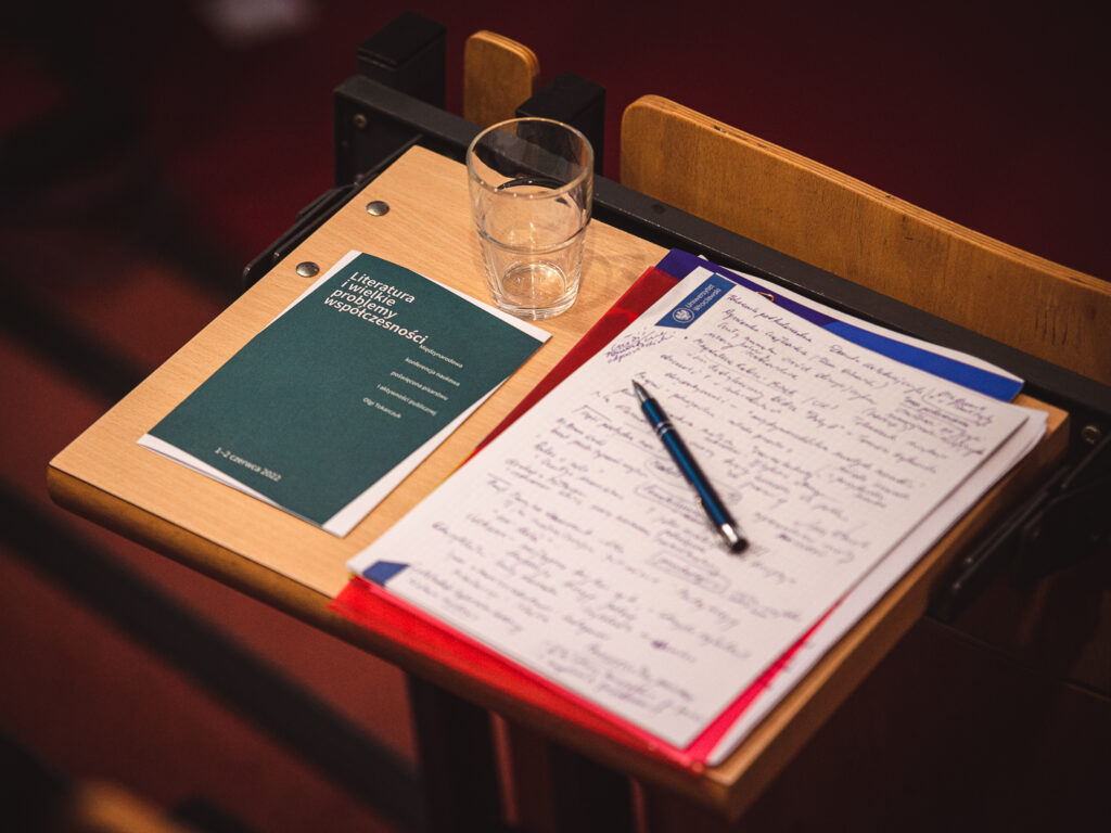 Na zdjęciu: szklanka, długopis, notatki i ulotka konferencji naukowej